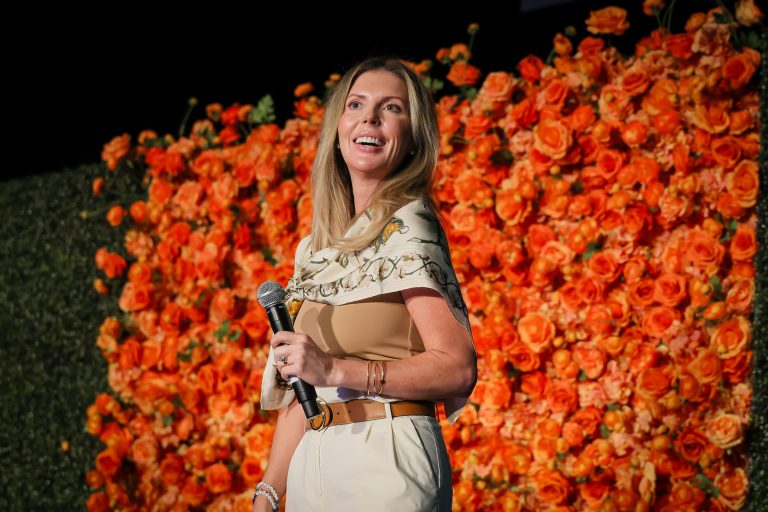 a woman holding a microphone in front of a wall of orange flowers